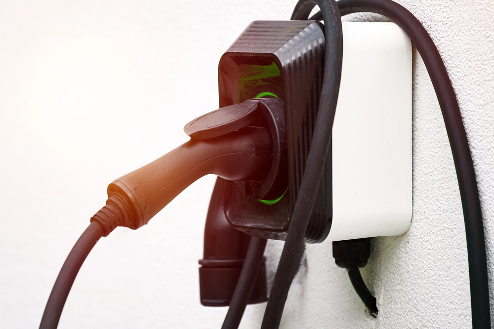 A black electric vehicle charging plug is inserted into a wall-mounted charging station, with cables wrapped around the device.