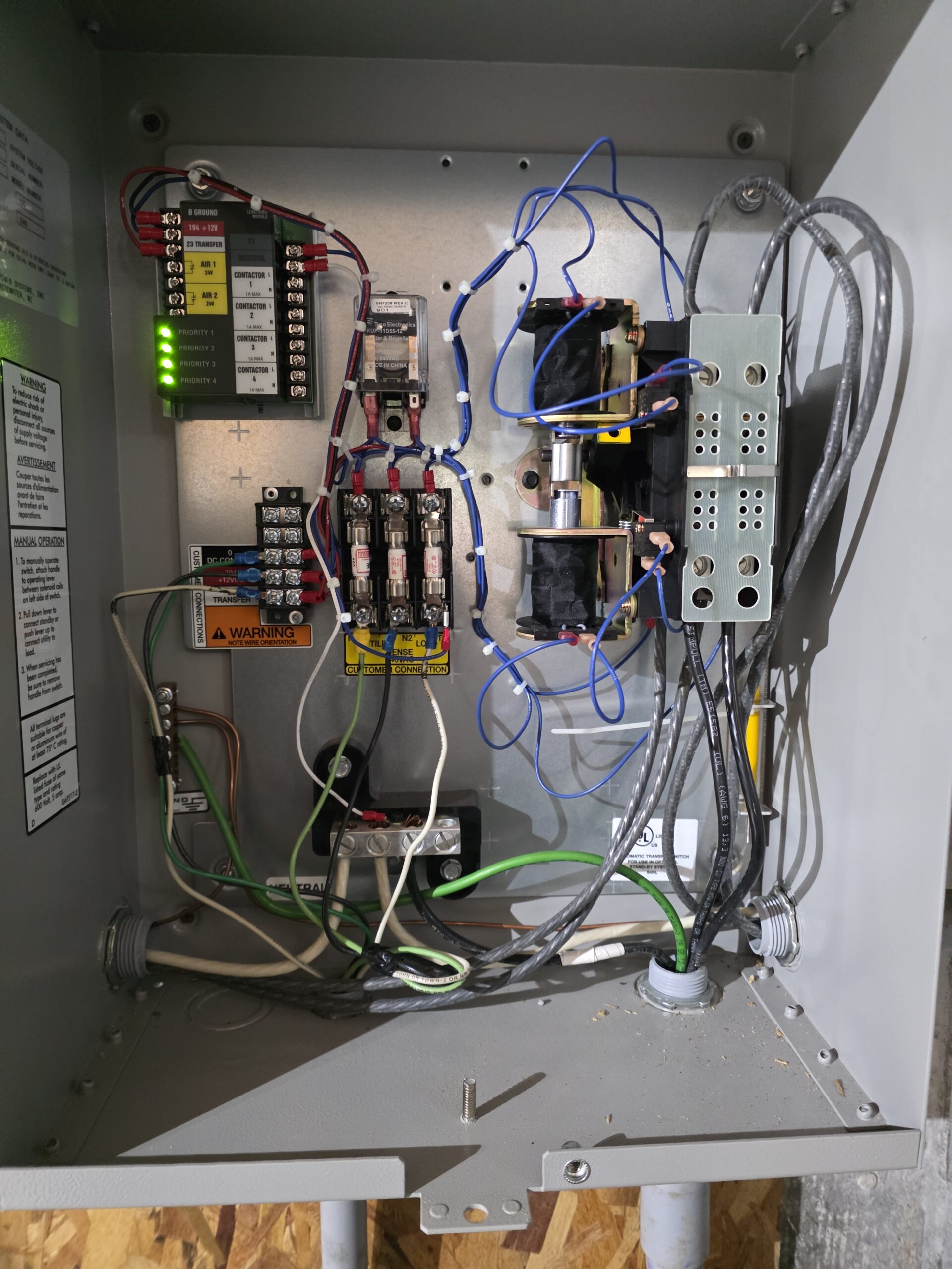 An open electrical control panel showing various relays, wires, terminal blocks, circuit breakers, and indicator lights.